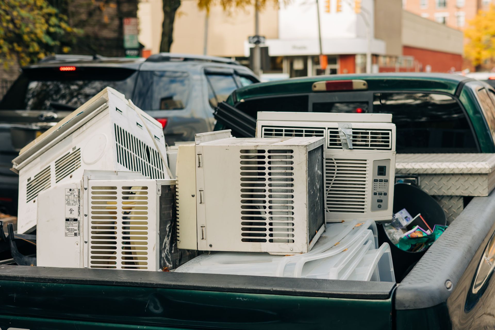 Several white air conditioners piled in the bed of a green pickup truck, parked outdoors.