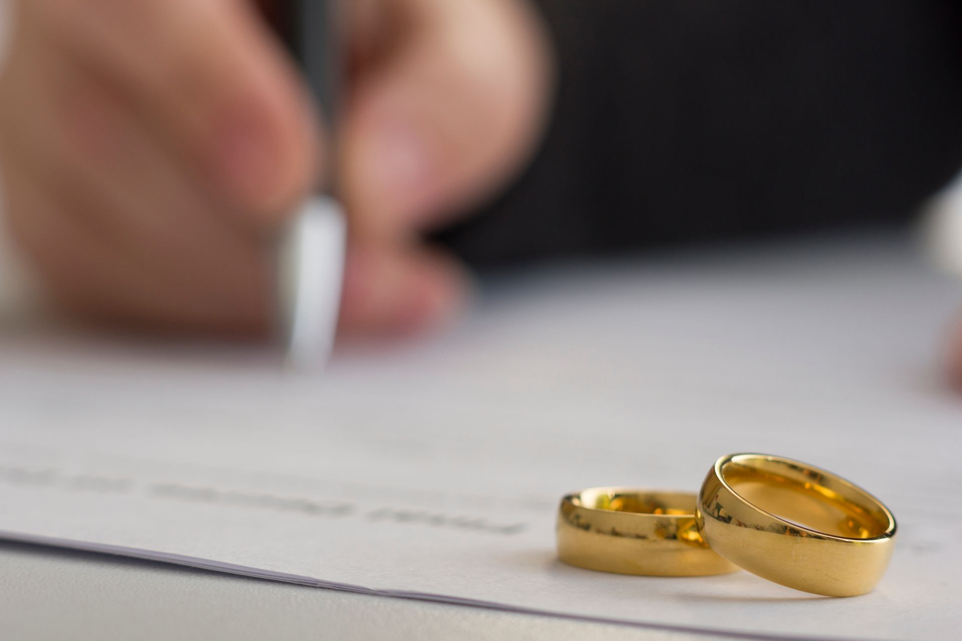 Wedding rings on document, hand signing with pen.