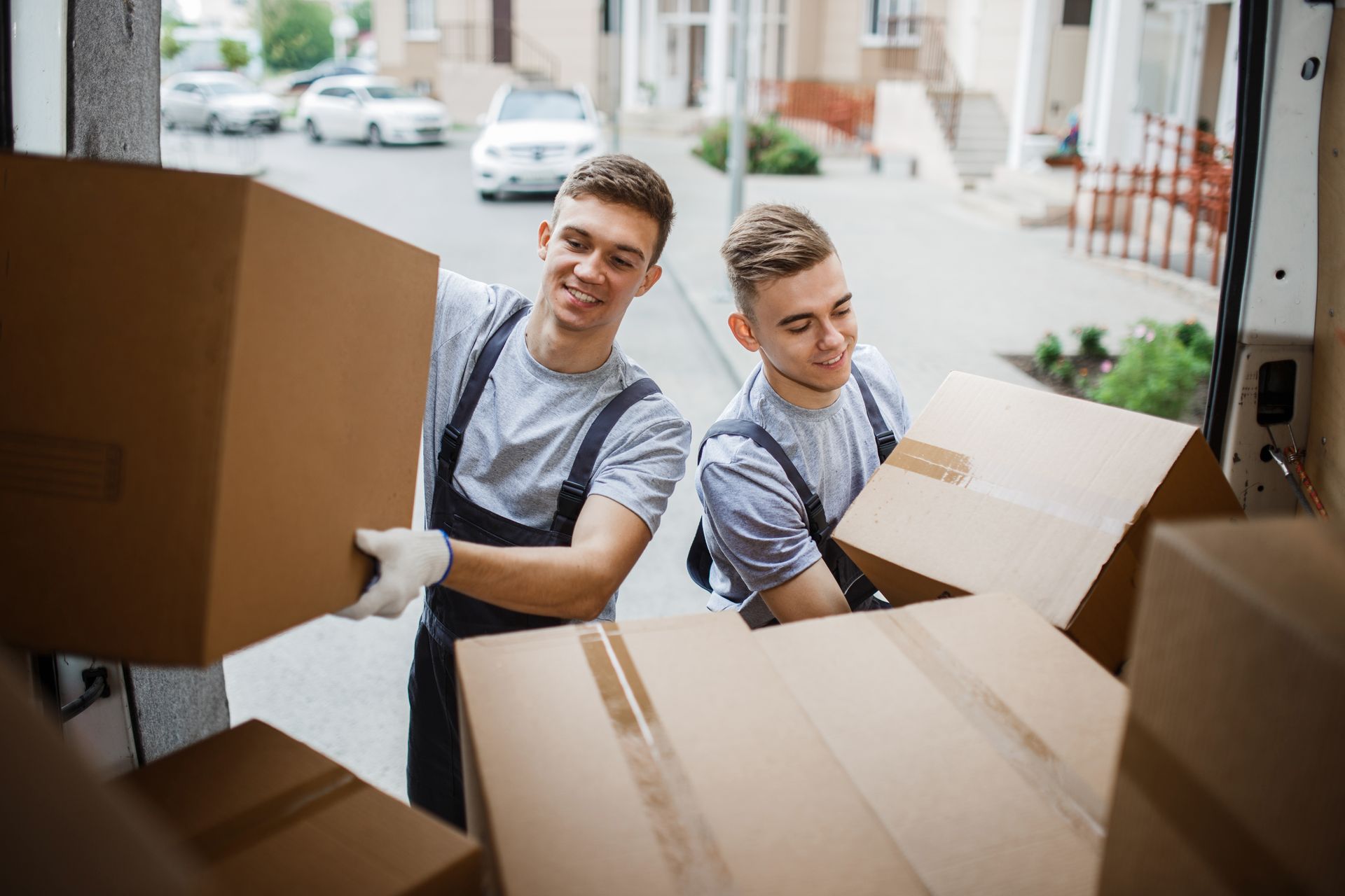 Two movers loading boxes into a truck, smiling in daylight.