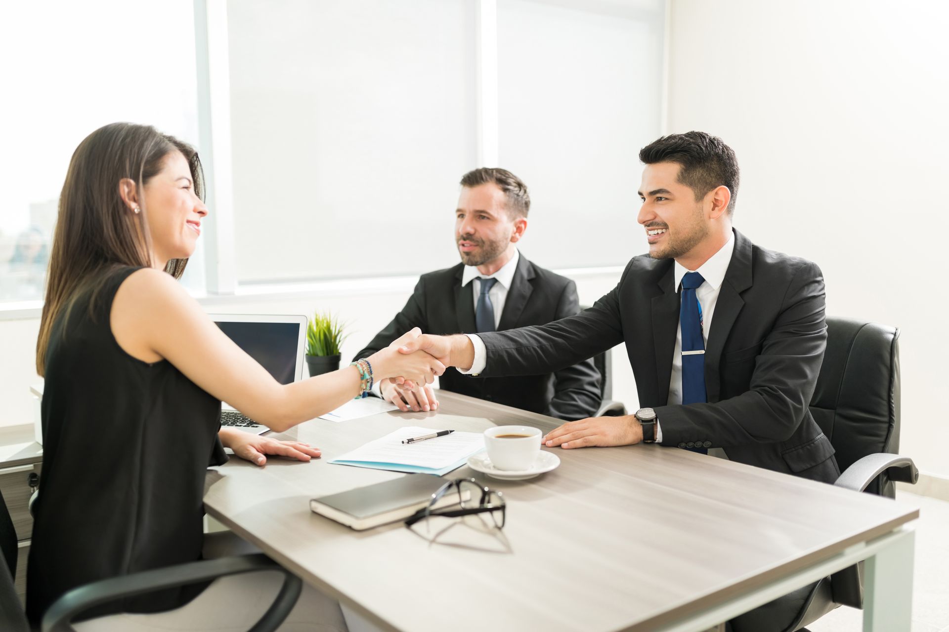 Woman shaking hands with a man at a table, two other people sitting with them in an office setting.