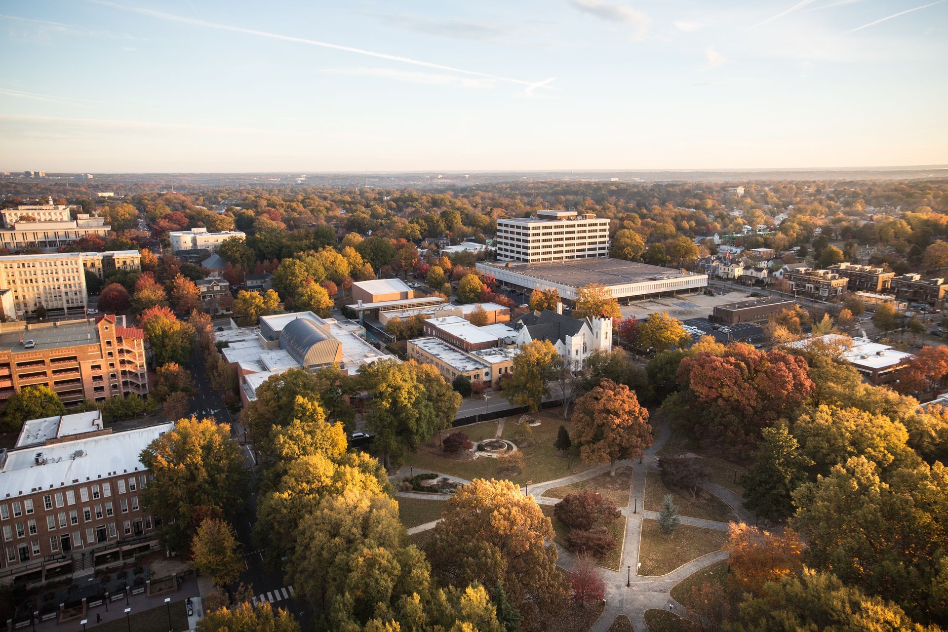 Aerial view of a city during autumn, with colorful trees, buildings, and a park, lit by golden sunlight.