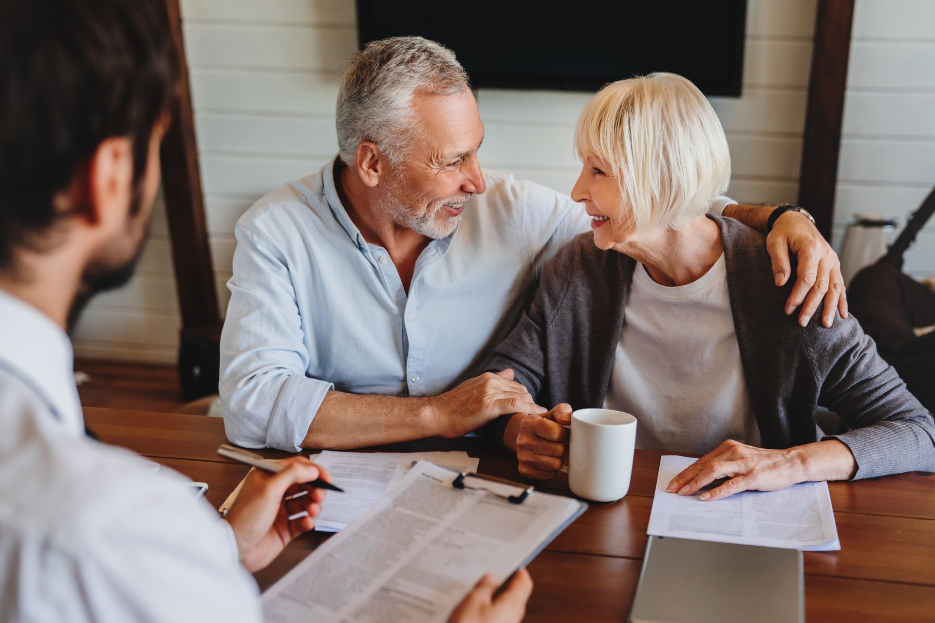 Older couple consults with a person about documents at a table. They are smiling, and one has an arm around the other.