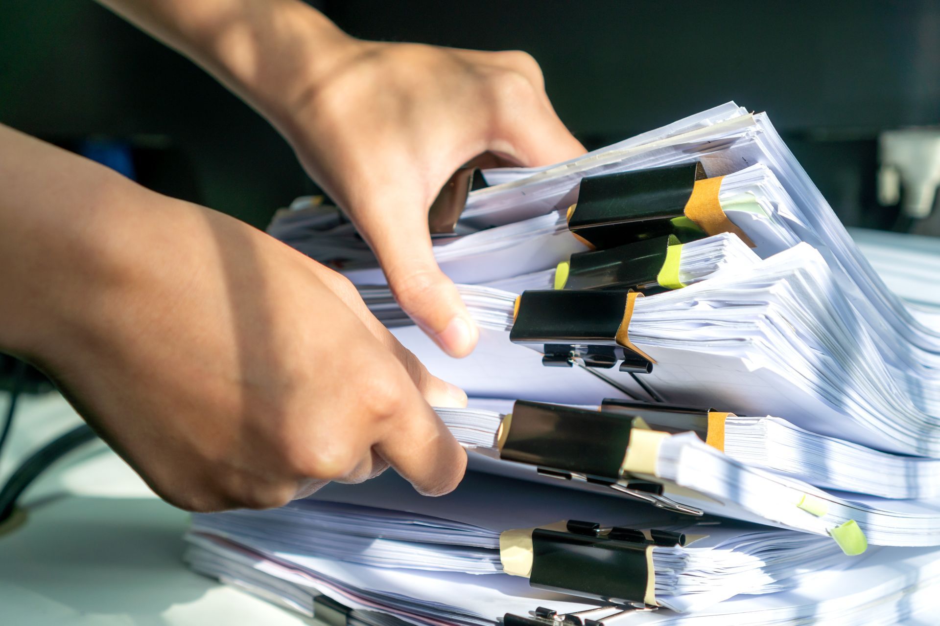 Hands sorting through a stack of paperwork secured with binder clips, likely in an office setting.