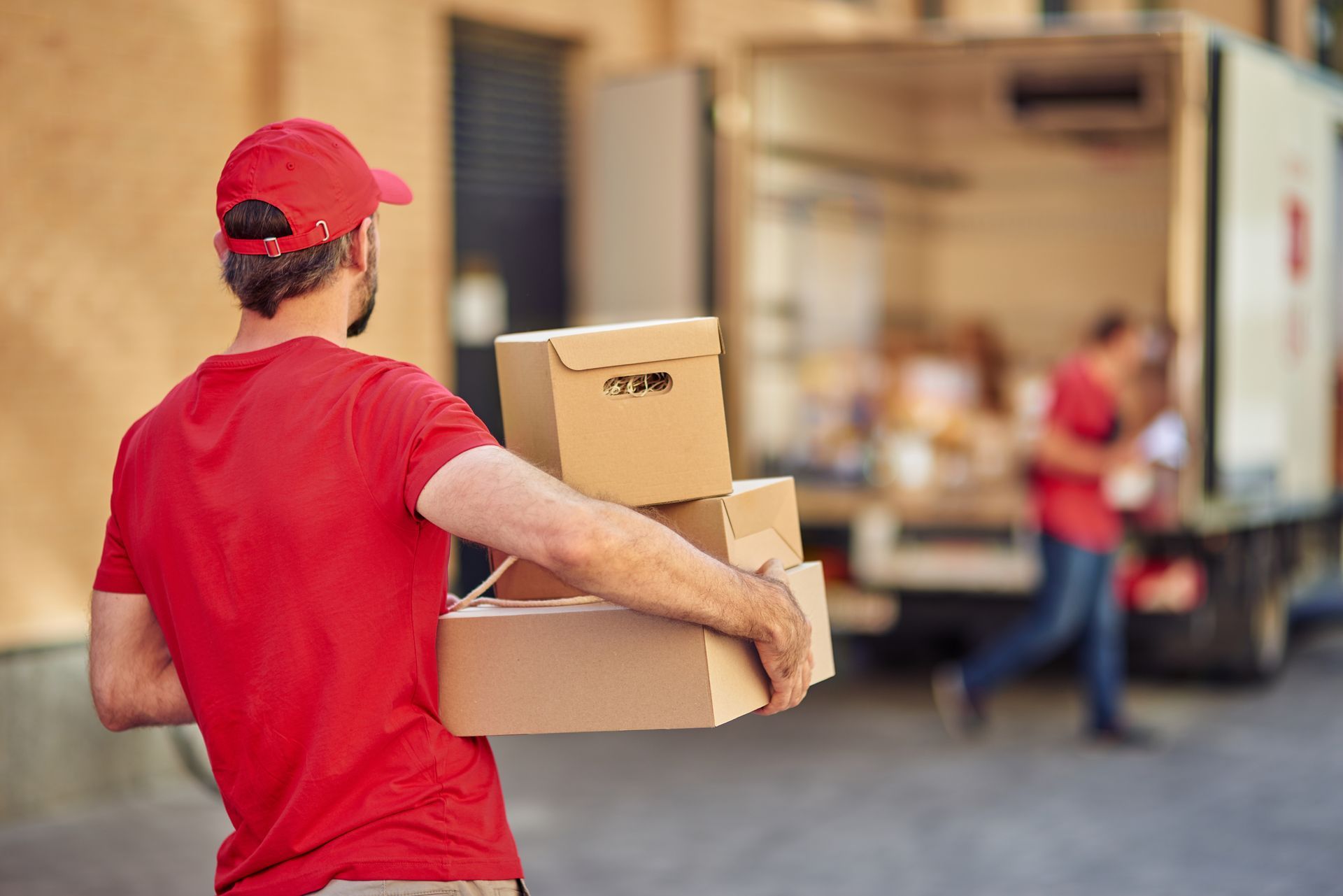 Delivery person in red carrying packages near a delivery truck.