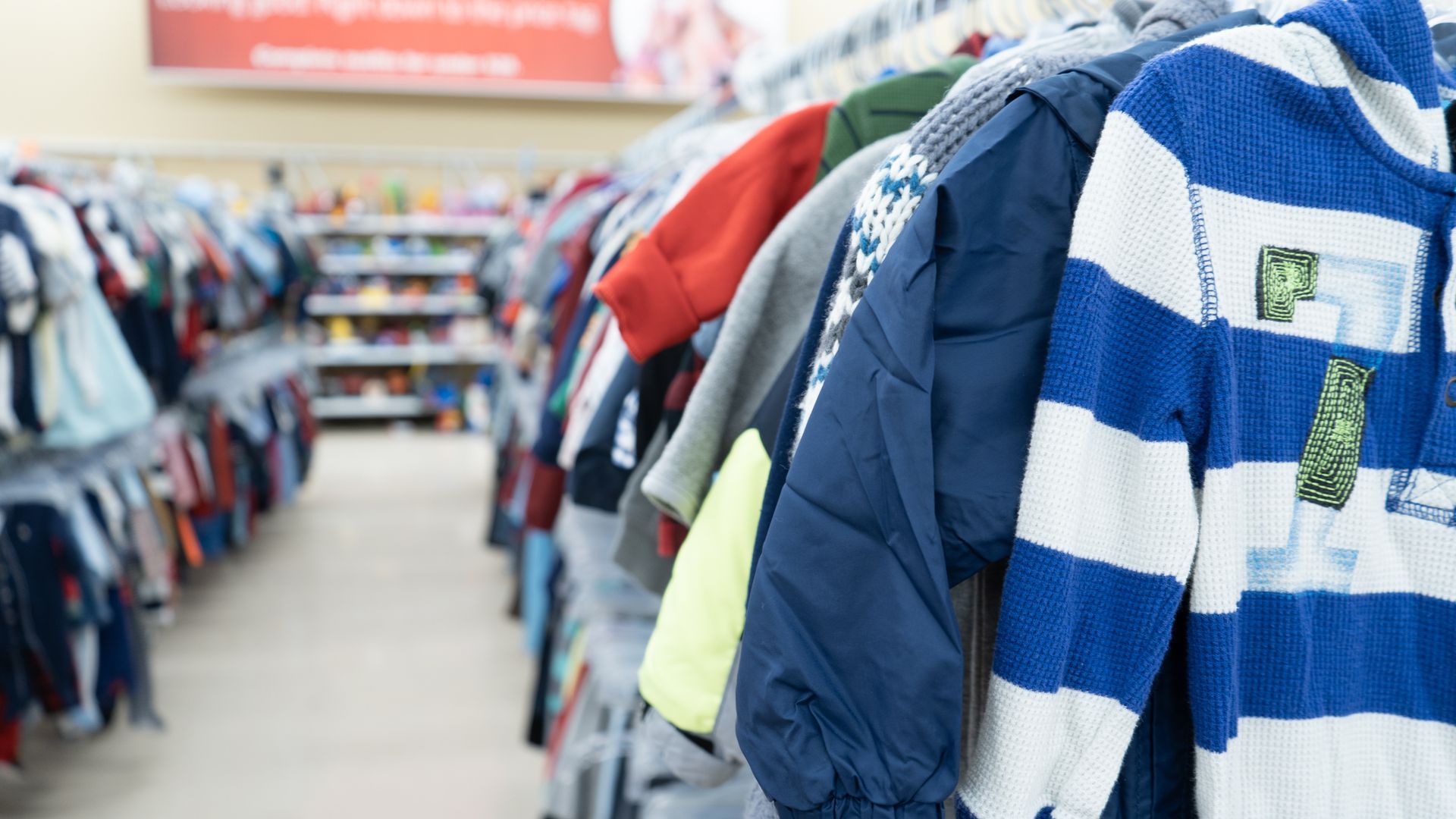 Rows of clothes hanging in a thrift store aisle. Jackets and shirts in various colors.