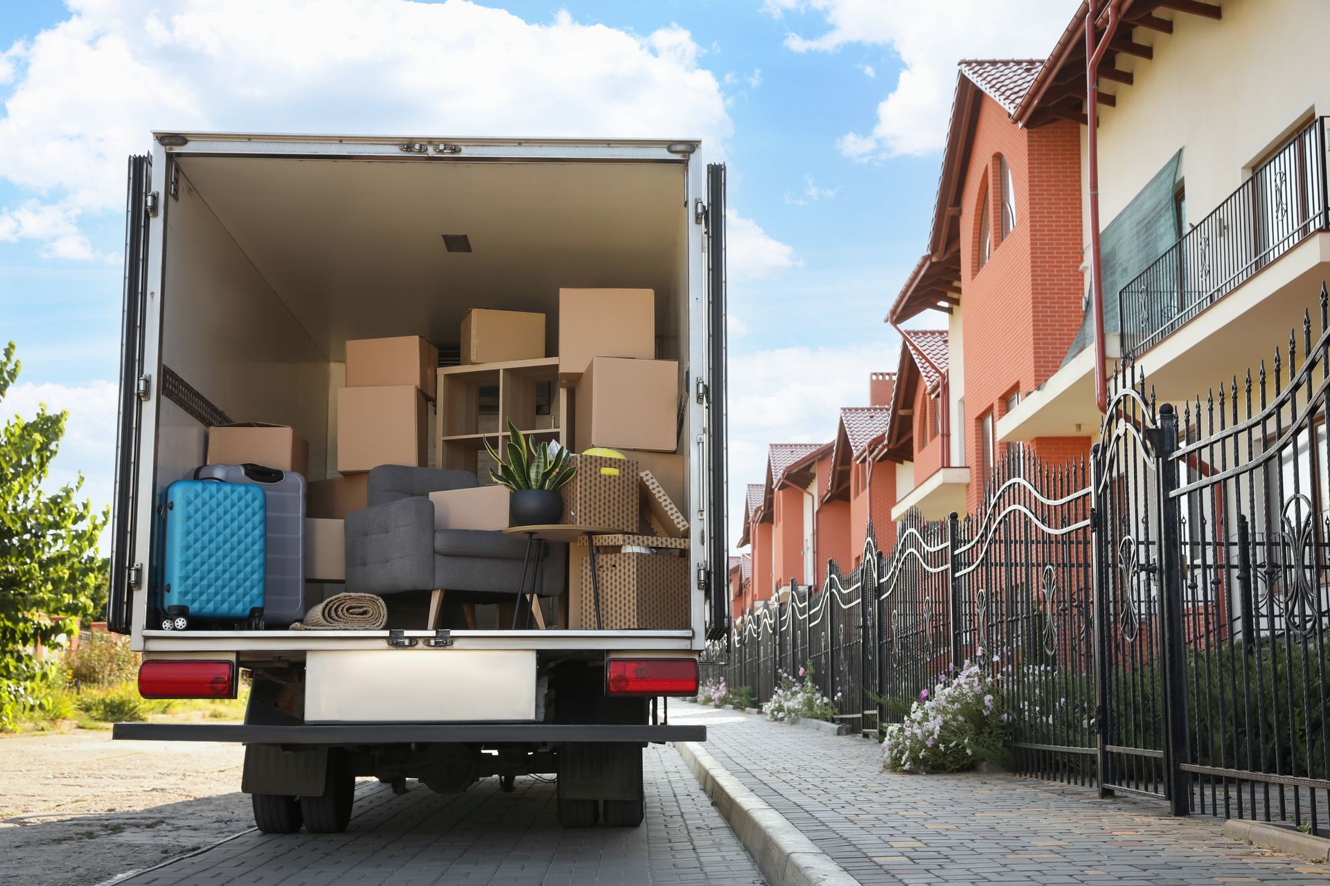 Moving truck loaded with boxes and furniture parked in front of brick houses.