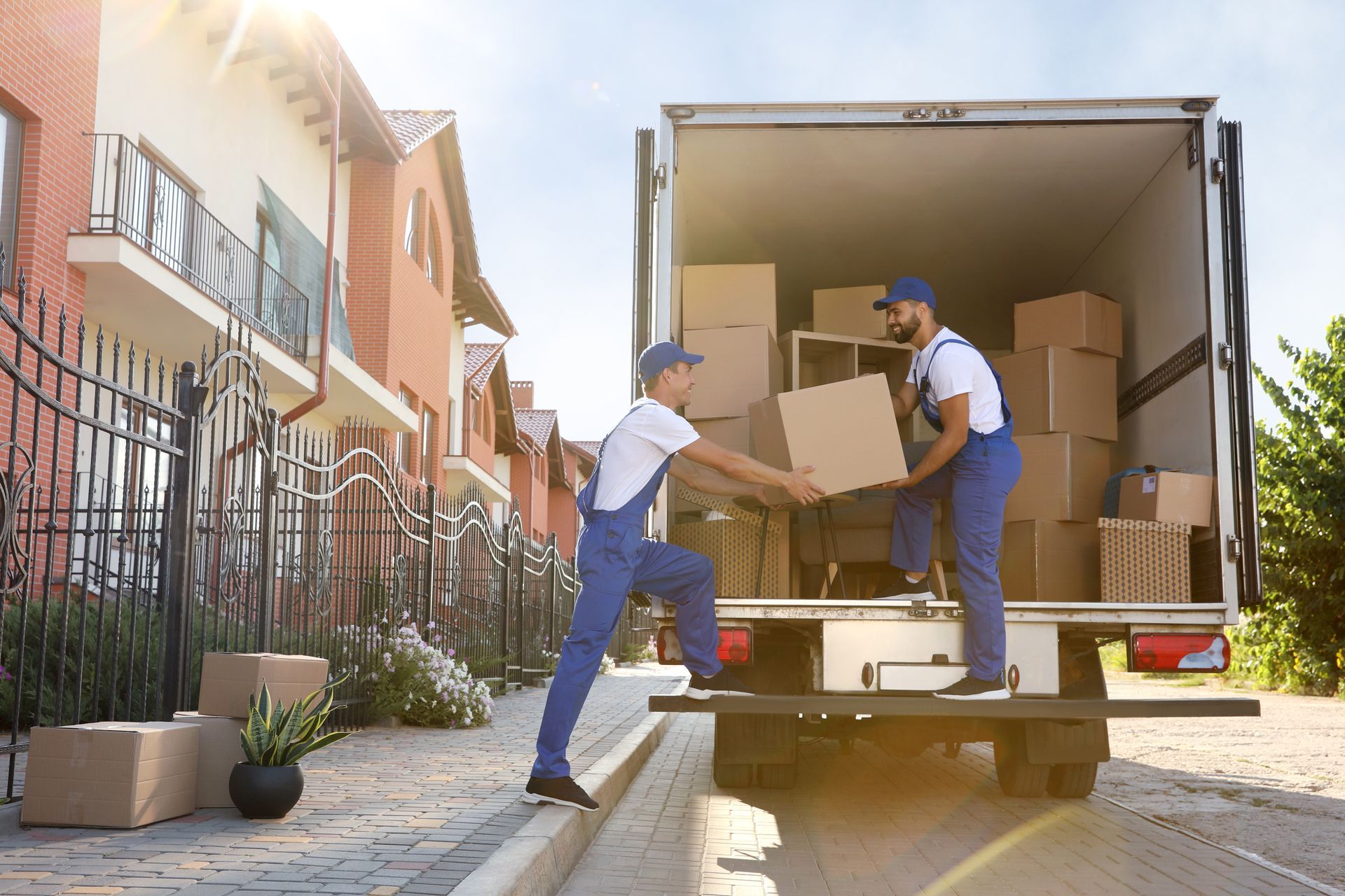Movers loading boxes into a truck, next to a brick house. Sunny day.