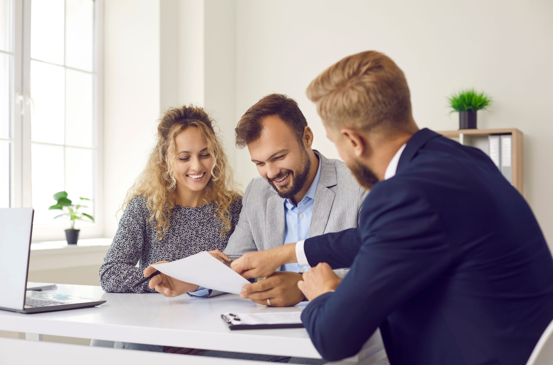 Couple reviewing paperwork with a professional in an office setting. They are smiling.