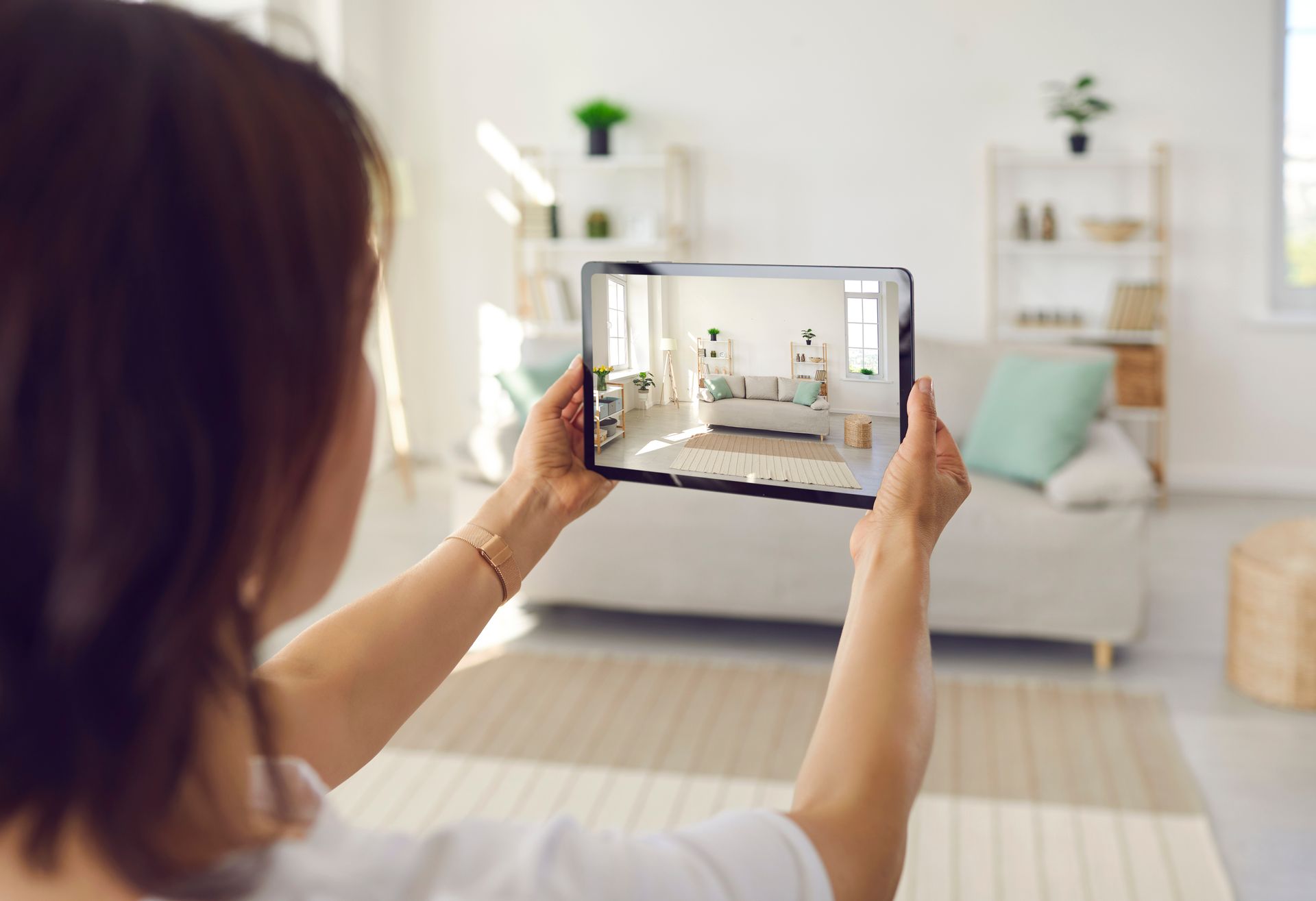 Woman holding a tablet, viewing a room with a sofa and decor.