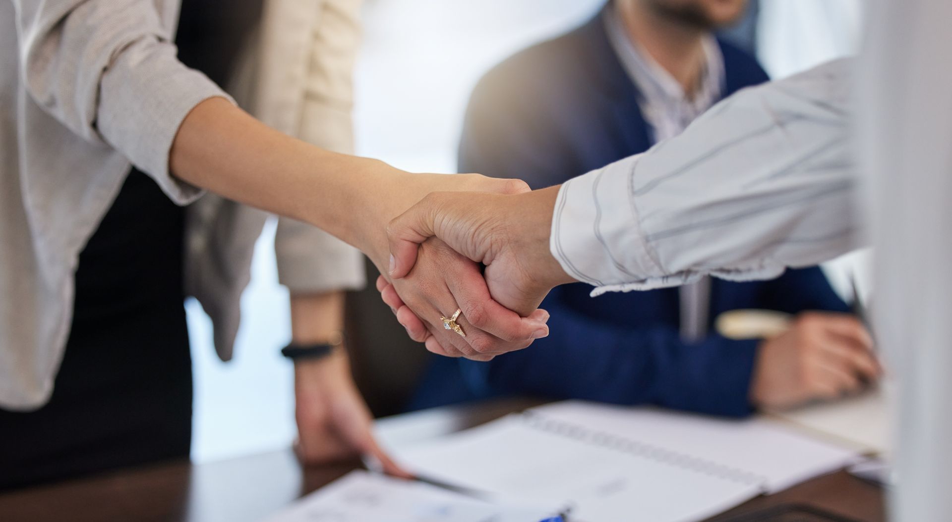 Close-up of three people shaking hands over a table with papers, likely sealing a deal.