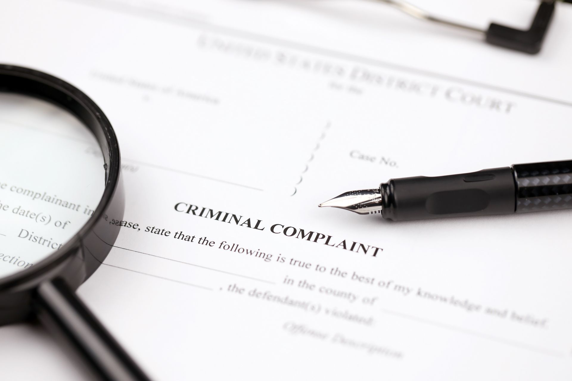 Magnifying glass on a criminal complaint form, with a pen, likely in a courtroom setting.