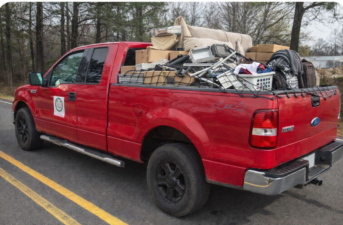 Red pickup truck filled with various items, possibly for disposal, parked on a road.
