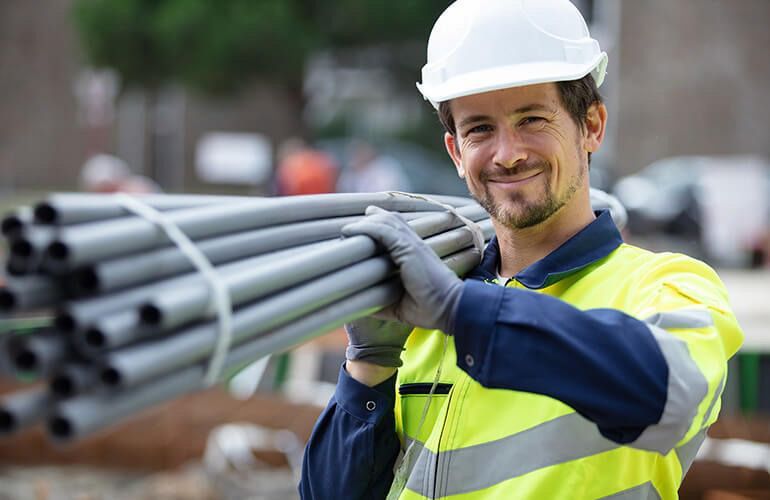 Construction worker in blue hard hat and safety vest, standing with arms crossed at a building site.