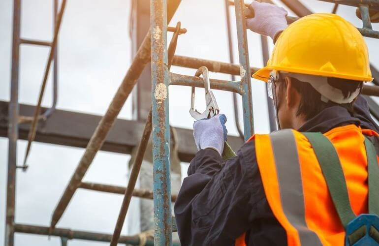 Construction worker in blue hard hat and safety vest, standing with arms crossed at a building site.
