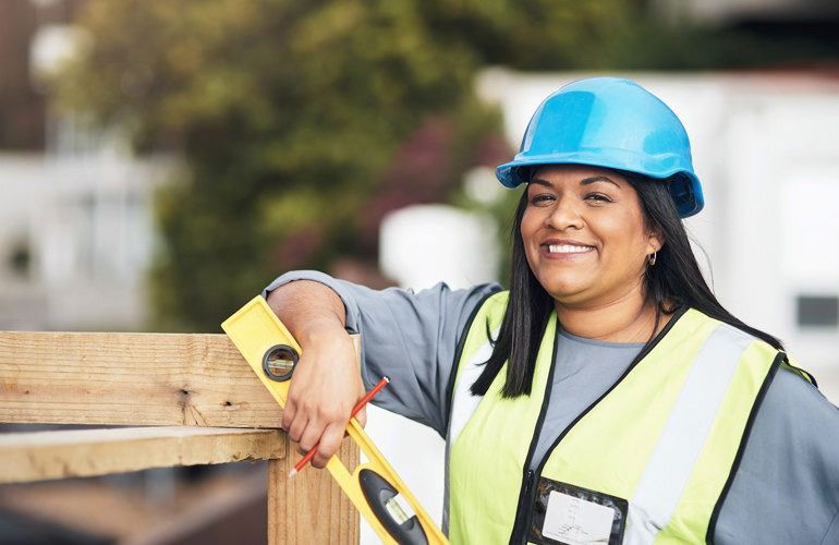 Construction worker in blue hard hat and safety vest, standing with arms crossed at a building site.