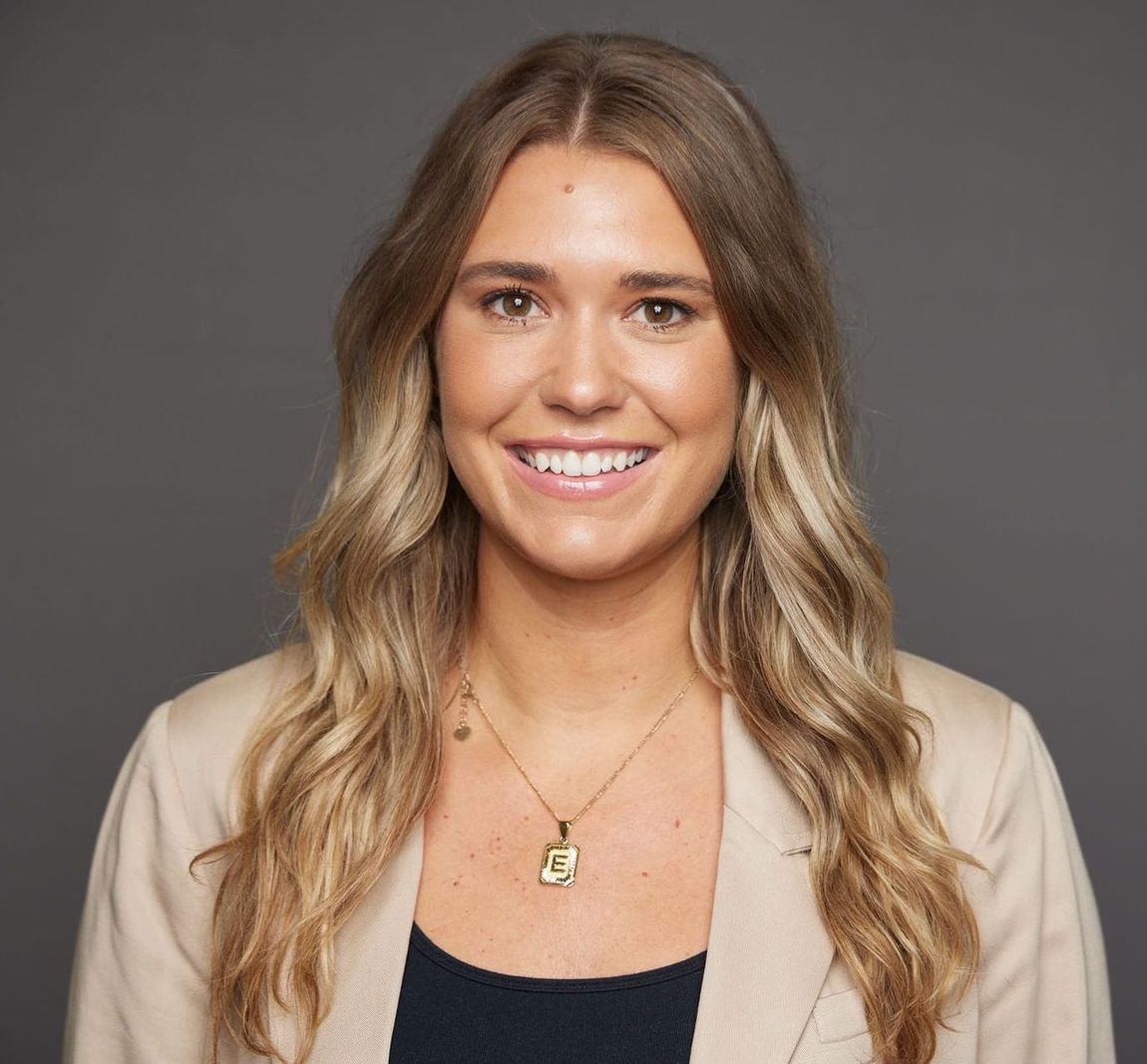 A woman wearing a necklace and a jacket is smiling for the camera.