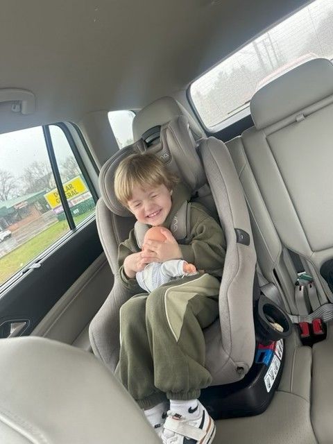 Blonde child smiling in a blue armchair with wooden legs, against a white wall.