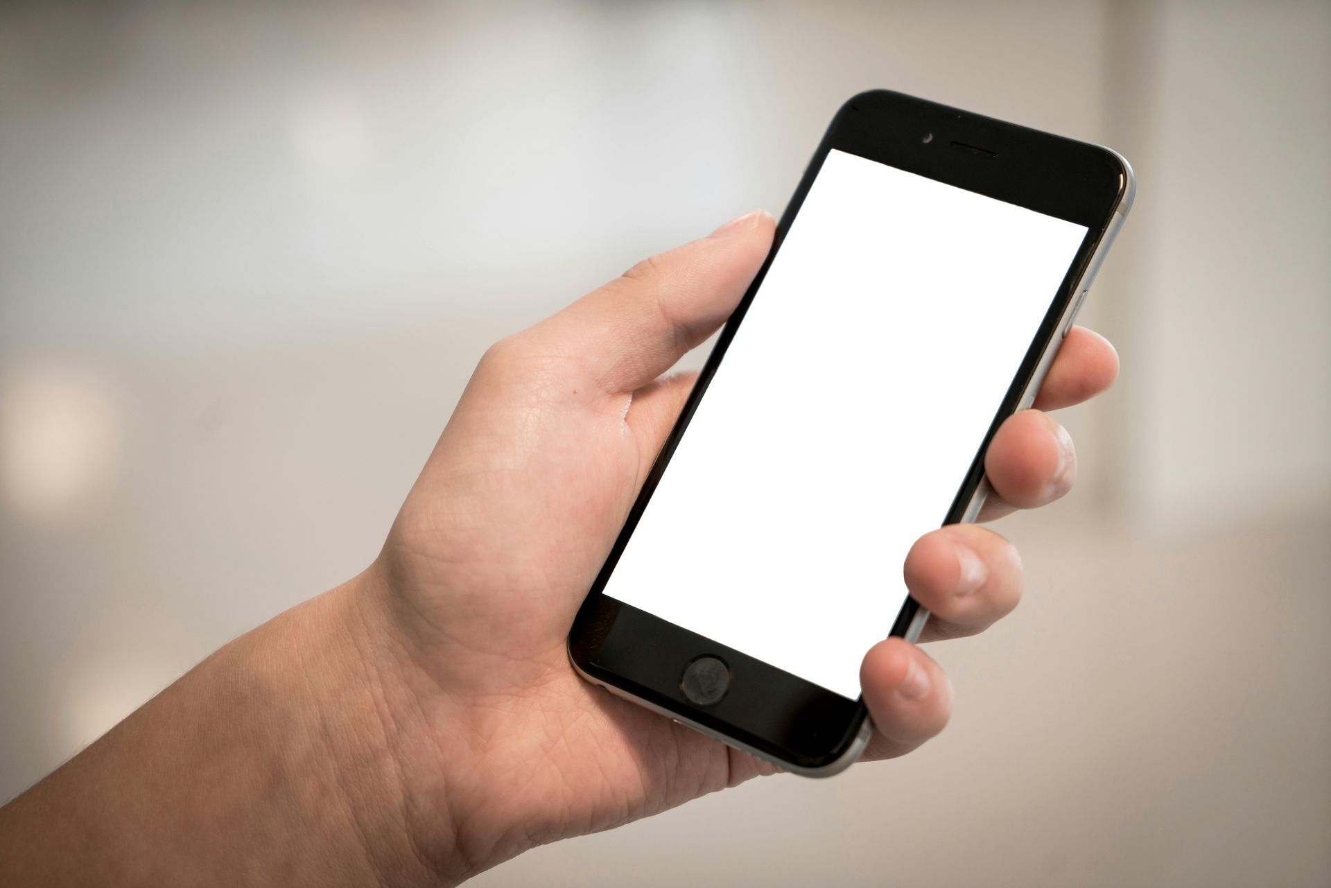 A hand holding a black smartphone with a blank white screen against a neutral, blurred background.