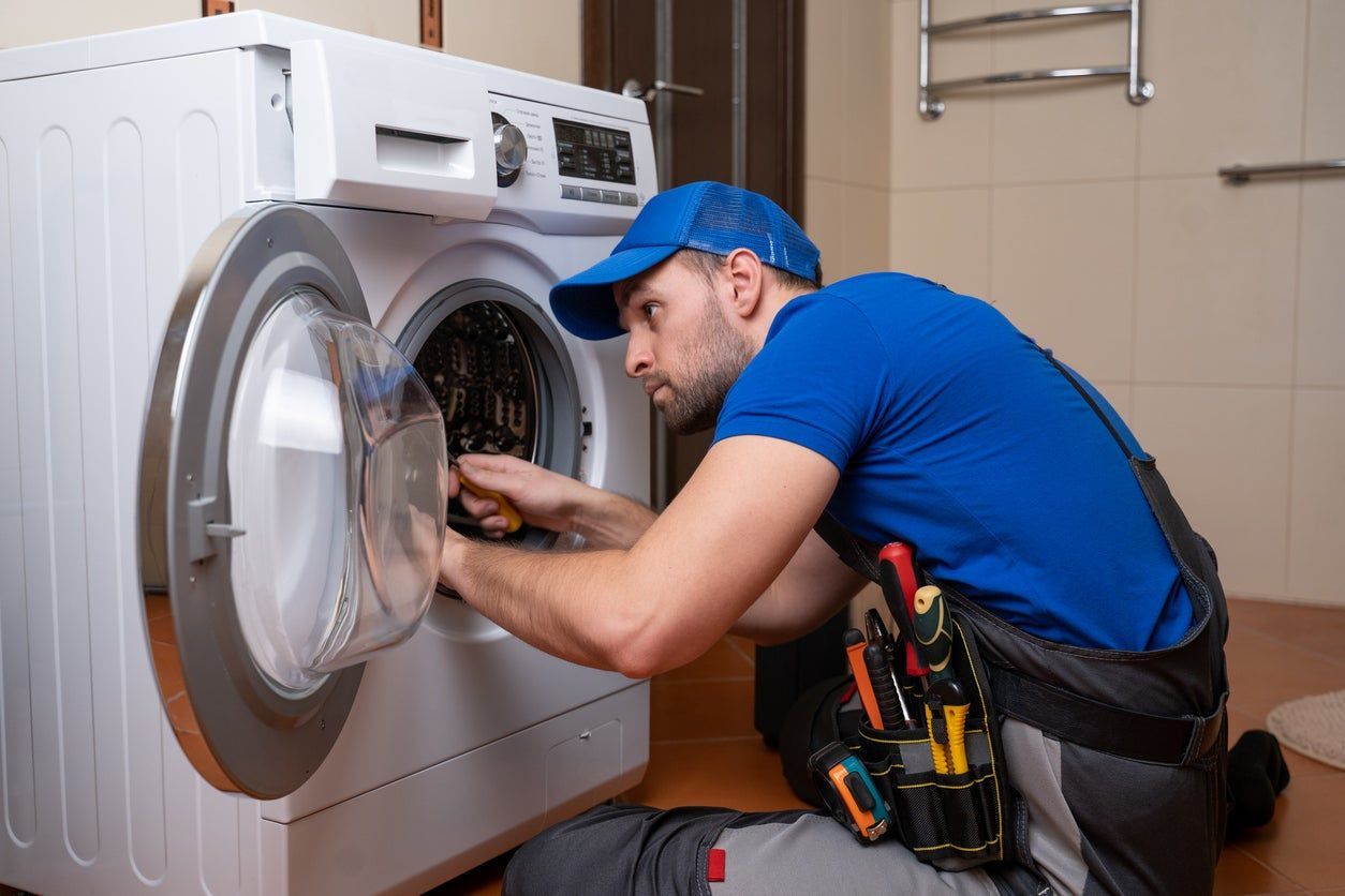 Technician in blue uniform repairing a front-loading washing machine in a laundry room