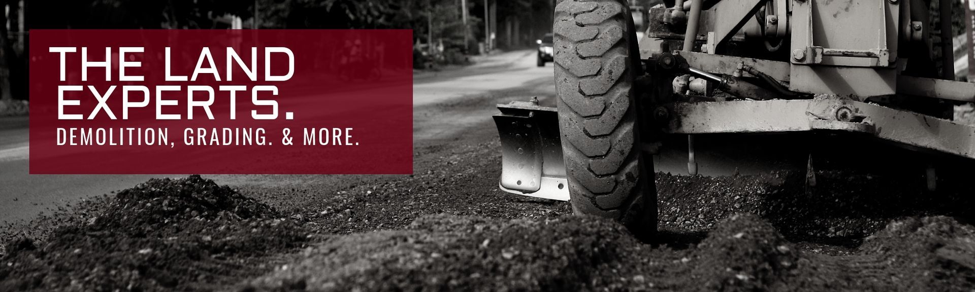 A close-up of a construction vehicle tire on dirt, with a red text box overlay that reads: THE LAND EXPERTS.