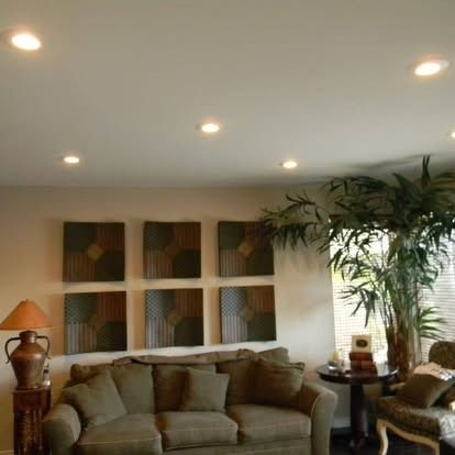 Living room with a brown sofa, a large potted plant, a side table with a lamp, and six framed square wall art pieces.