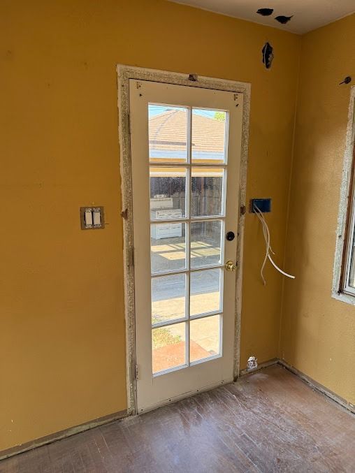 A white glass-paneled door set in a mustard-yellow wall of a room under construction with exposed electrical wires.