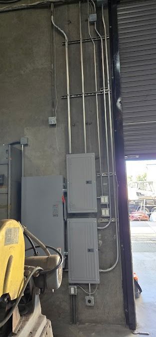 Electrical panels and conduit pipes mounted on a gray concrete wall inside a workspace.