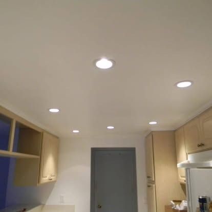 A view of a modern kitchen ceiling featuring multiple recessed round LED lights, with wooden cabinetry below.