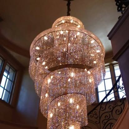 A large, multi-tiered crystal spiral chandelier illuminates a high-ceilinged interior with a staircase nearby.
