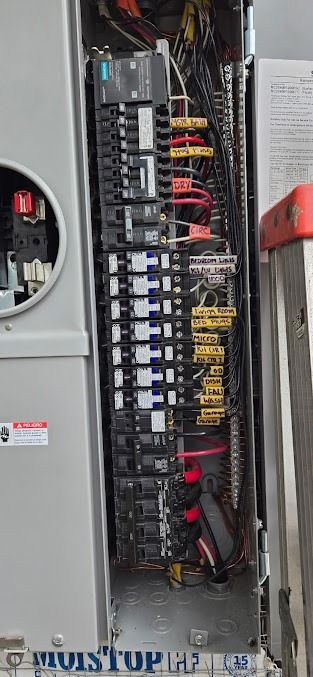 An open electrical breaker panel with multiple switches, colorful wiring, and a meter socket on the left.