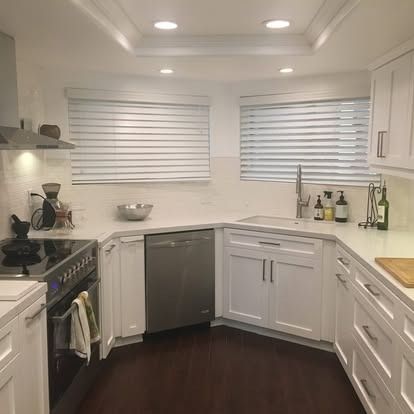 A modern kitchen with white cabinets, stainless steel appliances, white countertops, and dark hardwood floors.