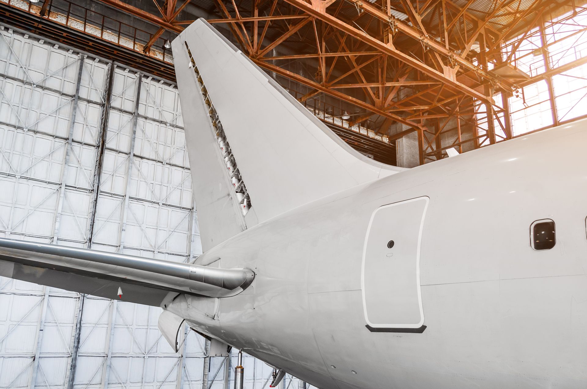 Tail section of a white airplane inside a hangar, showing the vertical stabilizer and tail.
