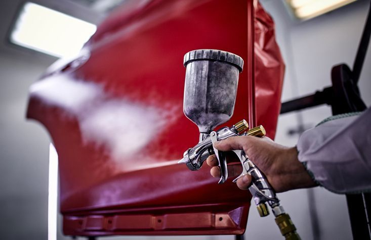 A person spraying red paint onto a car door with a spray gun in a paint booth.