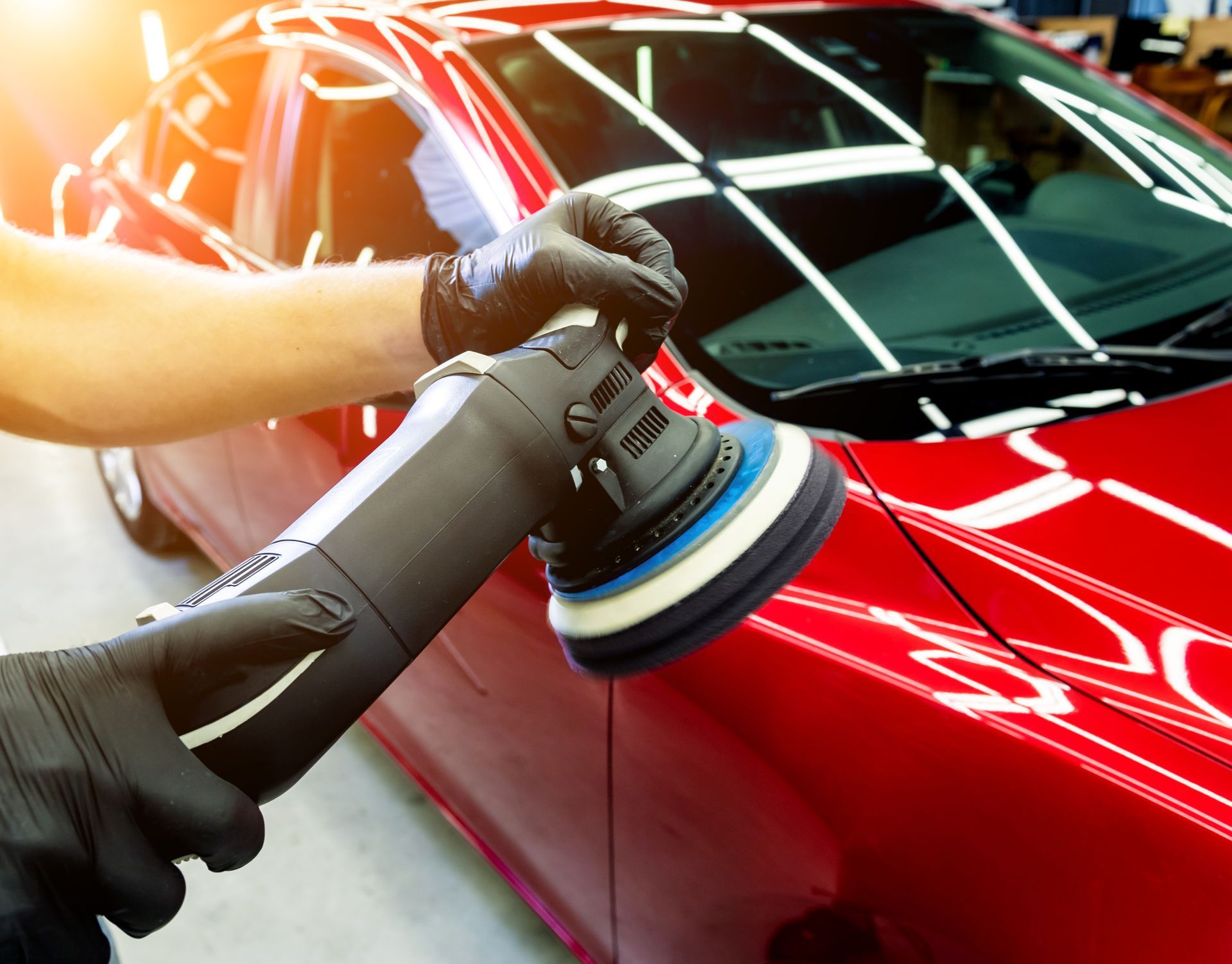 Hands wearing black gloves using a polisher on a red car's body.