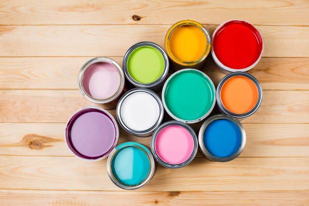 Open paint cans in various bright colors arranged on a wooden surface.