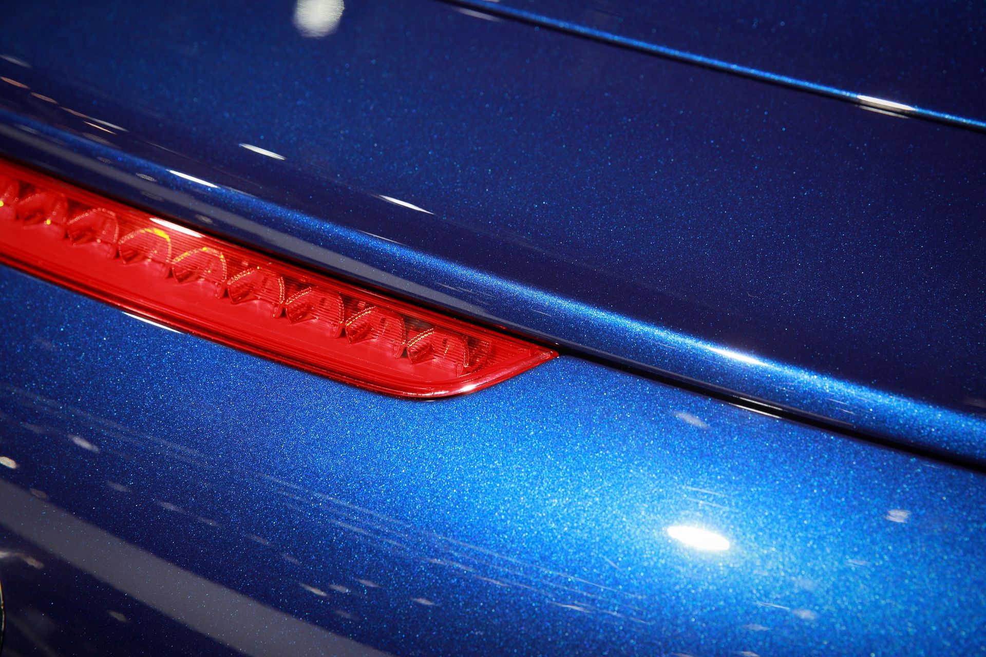 Close-up of a blue car with a red taillight. The paint has a metallic shimmer.