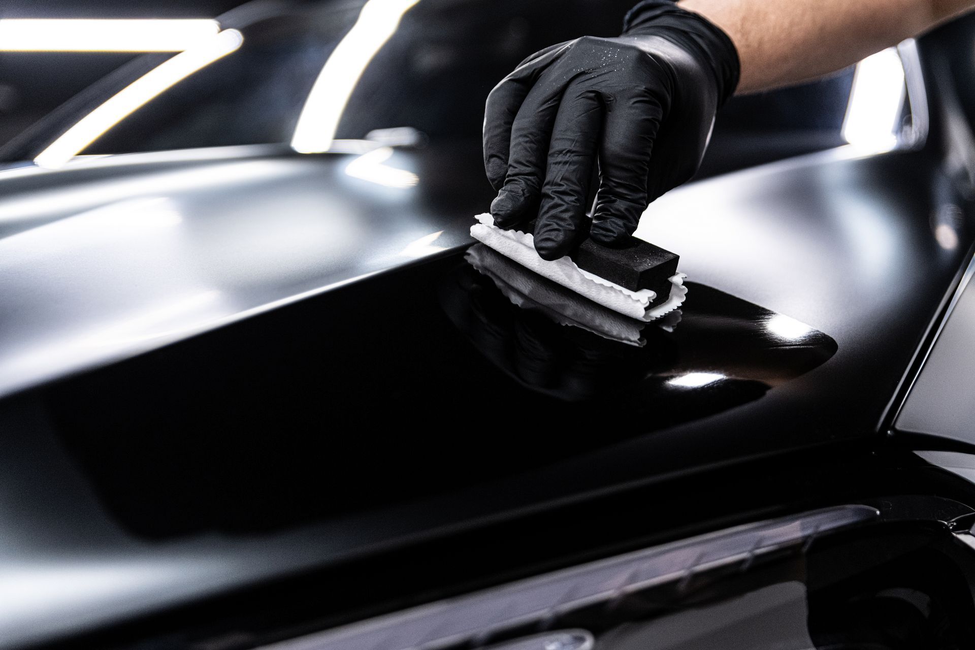Gloved hand applying a ceramic coating to a shiny black car surface.