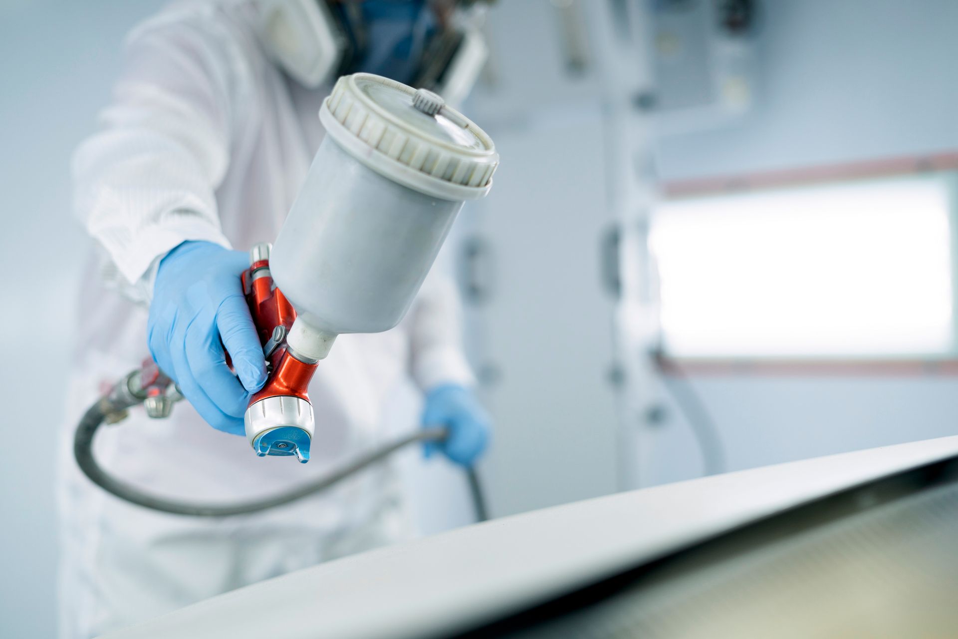 Person in protective suit spraying paint with a spray gun in a paint booth.