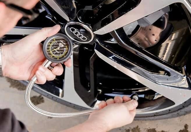 A man is checking the air pressure of a car wheel