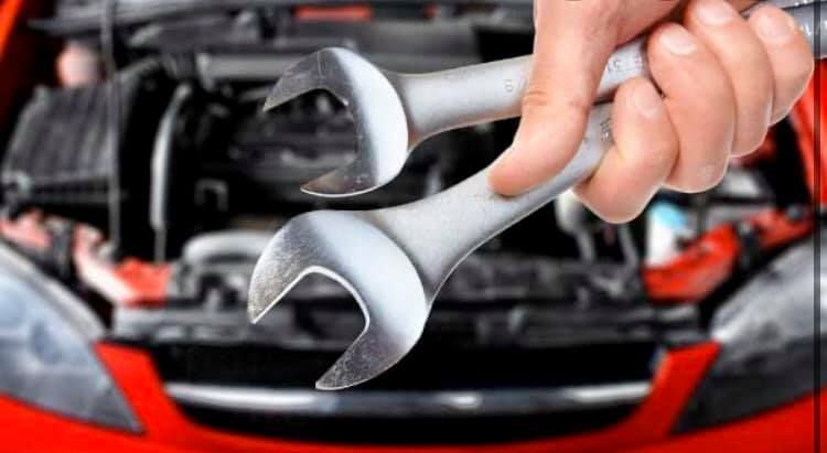 A person is holding a wrench in front of a red car.