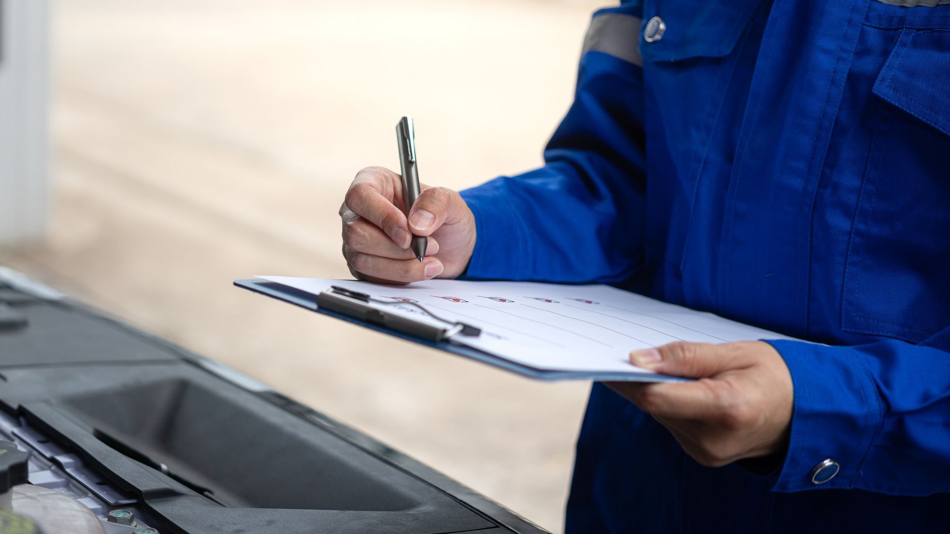 A mechanic is writing on a clipboard while standing next to a car.