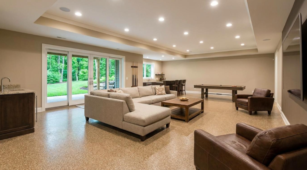 Spacious modern living room with beige sofas, recessed lighting, and large sliding doors to a green patio