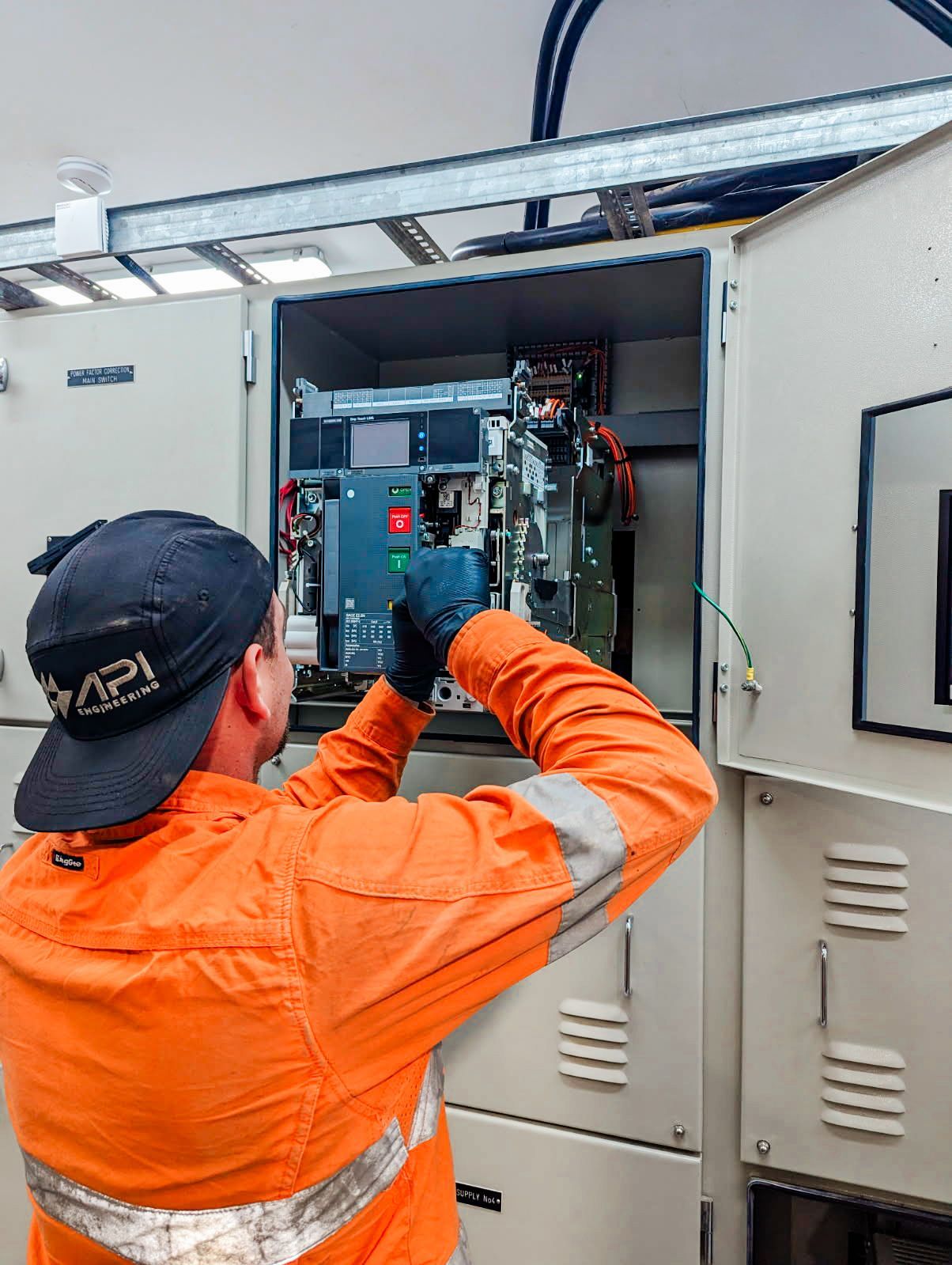 Electrician in orange workwear working on electrical panel.