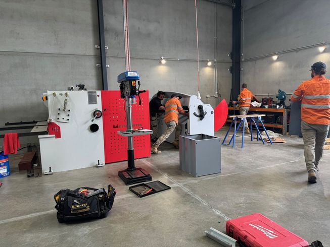 Workers assembling machinery in a workshop. Red and white machinery with workers in orange shirts.