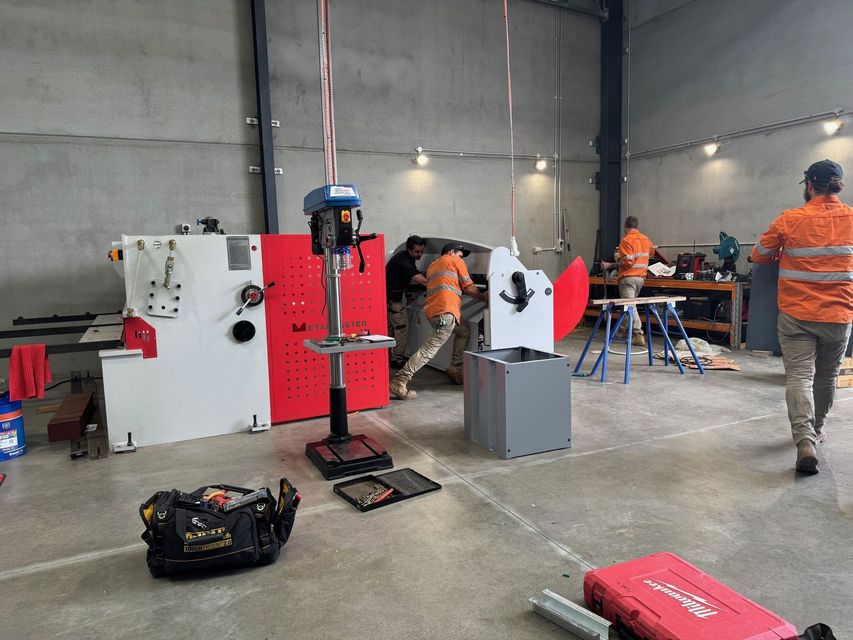 Workers assembling machinery in a workshop. Red and white machinery with workers in orange shirts.