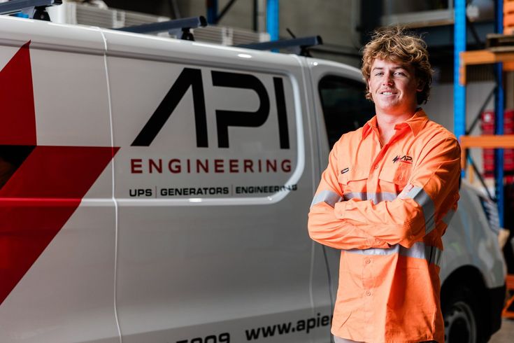Man in orange workwear stands next to a van with "API ENGINEERING" logo.