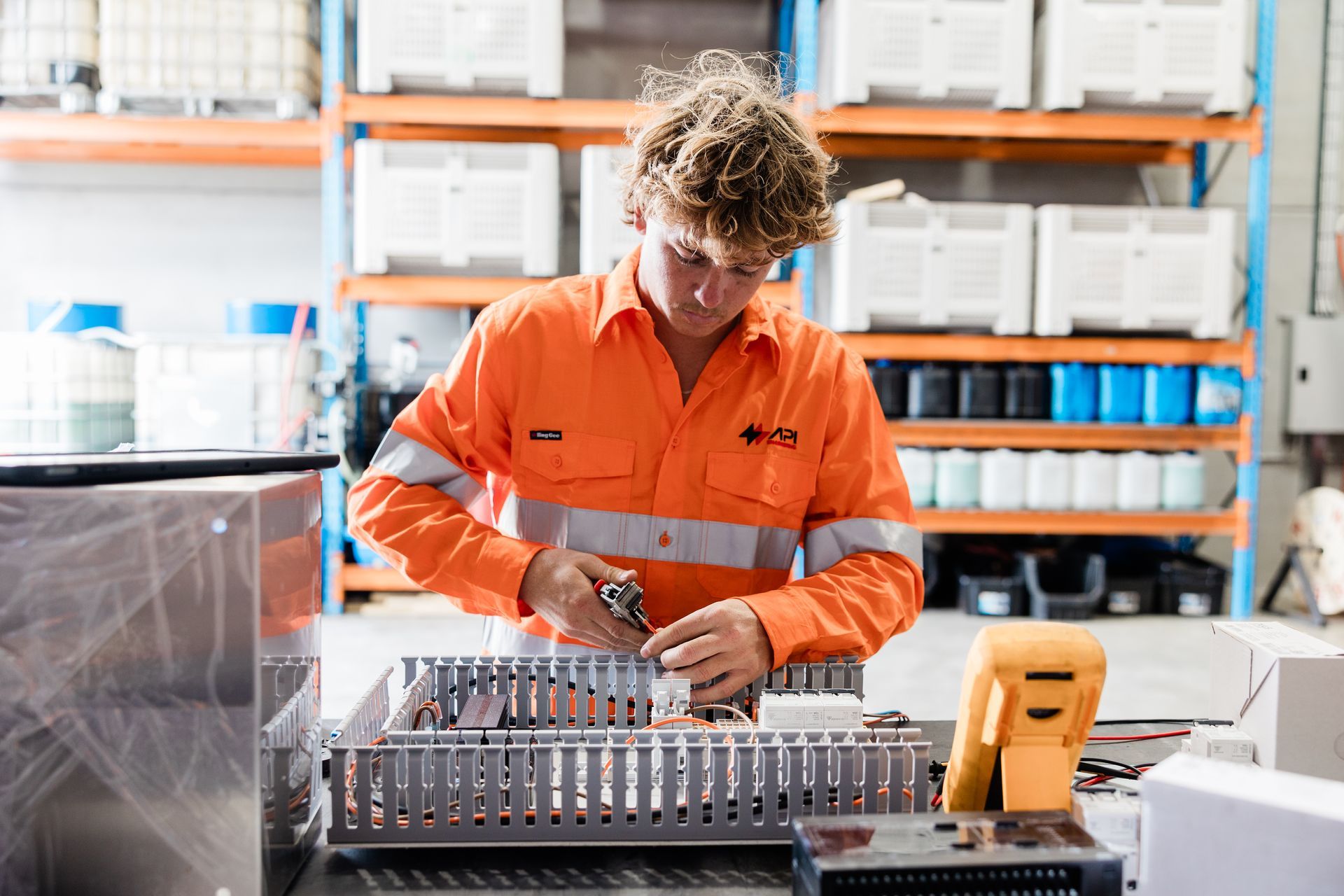 Person in orange work clothes working on electronics in a warehouse setting.  — API Engineering in Charmhaven, NSW