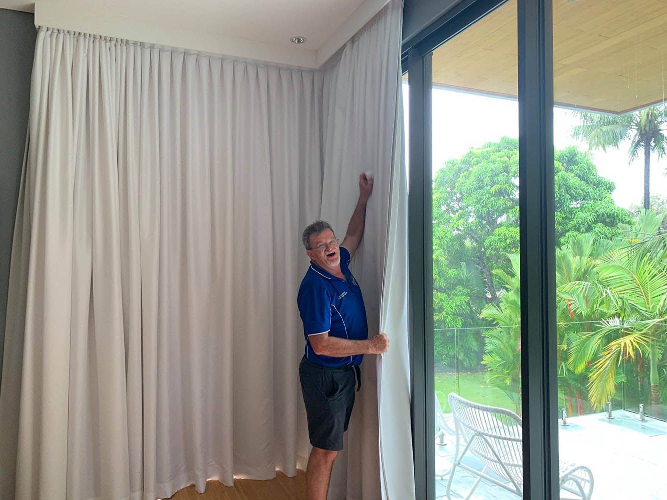 A Man is Standing in Front of a Sliding Glass Door Holding a White Curtain — Wow Clean Cairns in Bayview Heights, QLD