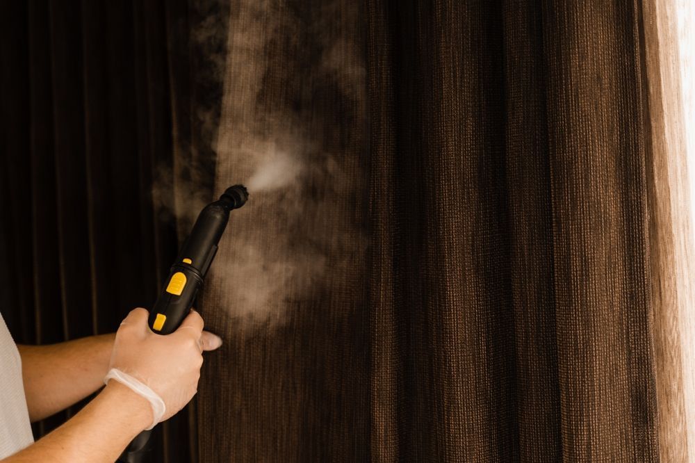 A Person Steam-Cleaning Vertical Blinds with A Handheld Steamer — Wow Clean Cairns in Stratford, QLD