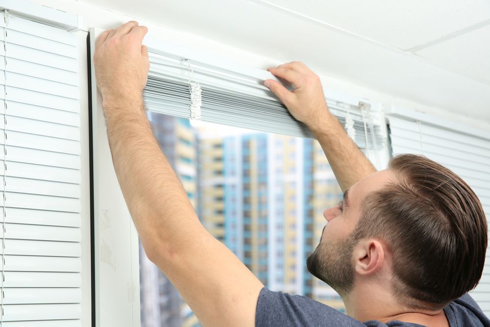 A Man is Installing Blinds on a Window — Wow Clean Cairns in Trinity Beach, QLD